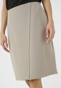 Een beige kokerrok tot de knie, met een soepele textuur, strakke lijnen en subtiele stiksels. Geen zichtbare hardware of patronen.