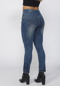 Užasne uske traperice u srednje plavoj denim boji s visokim strukom. Imaju cvjetne vezove na rubovima. Nosene s crnim čizmama na visoku petu.