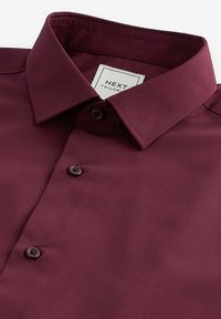 Cămașă bordeaux dintr-un material neted, cu un guler clasic, două butoane și o etichetă inscripționată "NEXT TAILORED."