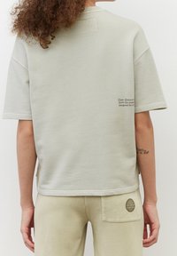 Felpa grigia chiaro oversize a maniche corte con colletto rotondo, caratterizzata da una piccola grafica testuale sul retro e una finitura texture.