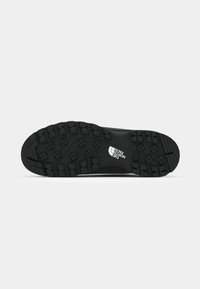 Black outdoor shoe sole with a textured design featuring deep treads for traction and a prominent brand logo.