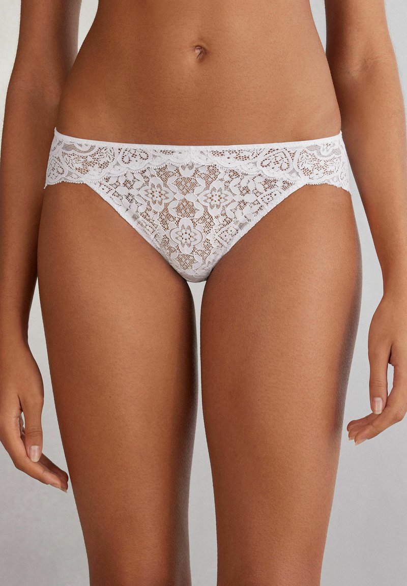 Witte kanten slipjes met bloemenpatronen, een scalloped tailleband en een zachte, doorschijnende textuur. Het ontwerp is delicaat en gedetailleerd.