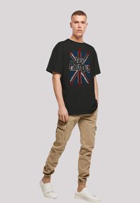 Black graphic t-shirt featuring a distressed print of the Union Jack and text "Sex Pistols." Paired with khaki cargo pants and white sneakers.