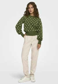 Groen gebreid truitje met witte stippen, ronde halslijn en geribbelde manchetten. Gepaard met crèmekleurige broek en witte sneakers.