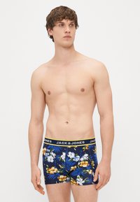 Zili ziedu bokseršorti ar dzeltenu jostu, uz kuras ir zīmols "JACK & JONES". Ziedu raksts ietver baltus un dzeltenus ziedus uz jūras zilā fona.