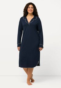 Camicia da notte navy in morbido tessuto, con maniche lunghe, colletto a patta e piping bianco lungo il colletto e i polsini; lunghezza al ginocchio con spacchi laterali.