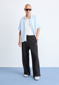 Lyseblå kortærmet skjorte, struktureret stof, båret over en hvid tanktop. Sorte løstsiddende sweatpants med et logo. Grå sneakers.