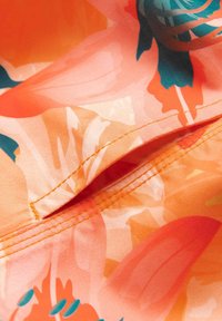 Gros plan sur un tissu floral orange et turquoise affichant une poche fendue cousue avec des lignes de couture détaillées.