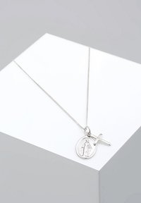 Sidabrinė vėrinys su apvaliu pakabuku, vaizduojančiu figūrą, kartu su mažuoju kryželiu. Grandinėlė plona, lygi.