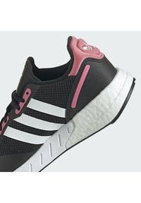 Zapatilla deportiva negra con parte superior de malla, franjas blancas, acentos rosas y una suela media blanca texturizada. Presenta un cuello acolchado y un sistema de cordones.