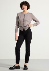 Cardigan marrone chiaro con scollo tondo, frontale con bottoni e polsini a coste, abbinato a pantaloni neri aderenti e mocassini neri.