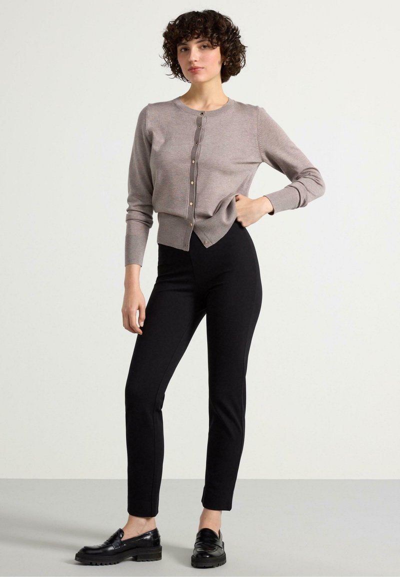 Cardigan marrone chiaro con scollo tondo, frontale con bottoni e polsini a coste, abbinato a pantaloni neri aderenti e mocassini neri.