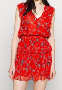 Rotes Blumenkleid mit V-Ausschnitt, Rüschenschultern und gestuftem Rock. Es weist auf einem durchsichtigen Stoff komplexe blaue und weiße Blumenmuster auf.