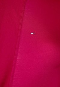 Skräddarsydd kortärmad skjorta i en livlig rosa tyg med en slät textur, med en liten broderad logotyp i blått, vitt och rött.