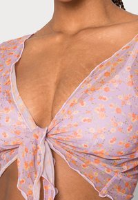 Fioletowa bluzka o kwiatowym wzorze z pomarańczowymi i różowymi akcentami. Lekki, przezroczysty materiał z węzłem z przodu i falbaniastymi brzegami.