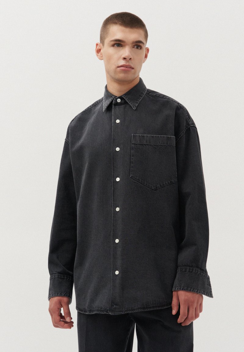 Zwarte spijkerblouse met een klassieke kraag, voorzak en knoopsluiting. De stof heeft een vervaagde textuur en een oversized pasvorm.