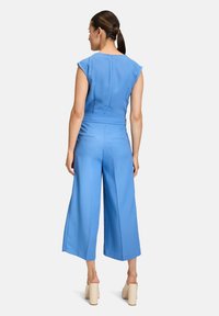 Blaue Jumpsuit mit weitem Bein, ärmellosem Design, tailliertem Oberteil und Reißverschluss hinten. Glatter Stoff ohne sichtbare Muster oder Akzente.