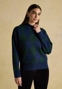 Tumesinine ja rohelise argyle-mustritega sviiter kõrge kaelusega, pikkade varrukatega ja soonikkoes hemiga, valmistatud pehmest, tekstureeritud kangast.