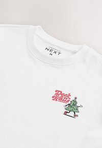 Balta T-krekls ar grafisku dizainu - karikatūru Ziemassvētku eglīti un tekstu "Deck the Halls" rozā krāsā, ar apaļu kaklu un īsām piedurknēm.