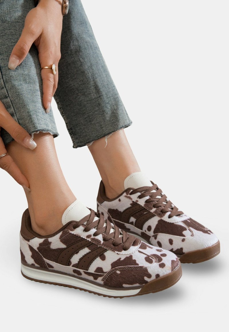 Baskets à imprimé vache marron et blanc avec des lacets et des accents marron, présentant une texture douce et un design à bout arrondi.