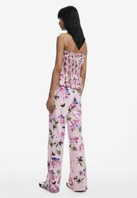 Top peplum floreale in rosa con spalline regolabili, abbinato a pantaloni a gamba larga caratterizzati da un vivace motivo floreale e farfalloso.