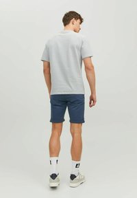 T-shirt a righe grigie e bianche abbinato a pantaloni corti blu navy. I pantaloni corti hanno i risvolti e l'outfit è completato da sneakers bianche e calzini.