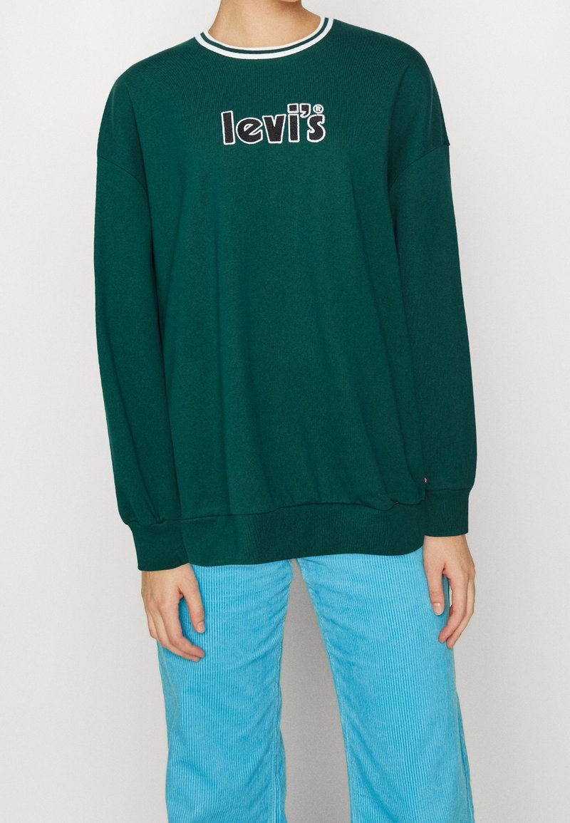 Felpa verde con collo a coste, con il logo "Levi's" ricamato in nero. Abbinata a pantaloni in velluto a coste azzurri.