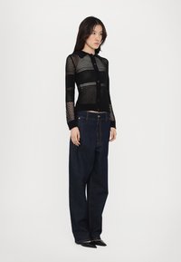 Black knit cardigan with a textured open weave, featuring a collar and button closure, paired with loose-fitting dark denim pants.