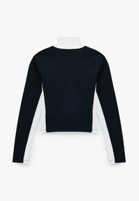 Top de manga larga en blanco y negro con un cuello alto. Presenta un diseño recortado. Textura suave, con paneles de mangas en blanco que contrastan.