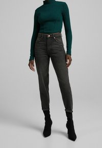 Mörkgrå jeans med hög midja och avsmalnande ben, med uppvikta fållar och framfickor, kombinerade med en ribbad grön polotröja.