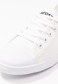 Baskets en toile blanches avec un capuchon en caoutchouc, un dessus texturé, six œillets et un logo brodé sur la languette. Forme arrondie et semelle plate.