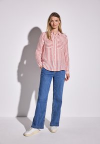 Knapplistad skjorta med röda och vita vertikala ränder, med två bröstfickor. Matchad med ljusblå raka jeans och vita sneakers.