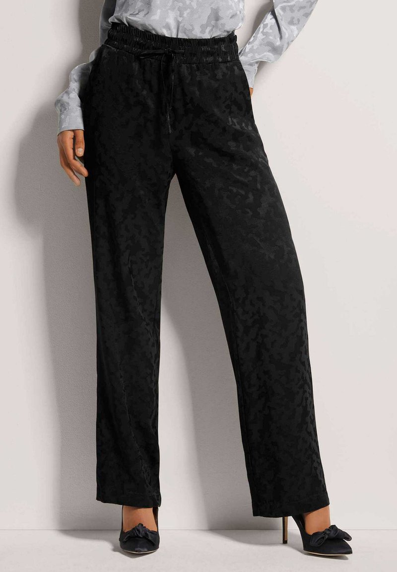 Zwarte wijde broek met een subtiel ton-sur-ton camouflagepatroon, met een elastische tailleband en een trekkoord. Soepele, lichte stof.