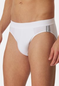 Białe męskie majtki typu slip z miękką gumką i subtelnym szarym akcentem. Materiał wydaje się lekki i ma gładką strukturę.