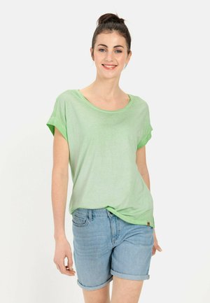 Lys grøn kortærmet T-shirt med rund halsudskæring, parret med opsmøgede denim shorts. Stoffet ser blødt og letvægts ud.