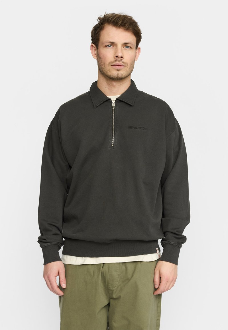 Donkergrijze pullover met een ritskraag, gemaakt van zachte stof. Heeft ribgebreide mouwen en onderrand, en een geprinte "REVOLUTION" logo op de borst.