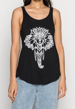 Black sleeveless top with white intricate elephant head design worn by a woman paired with light blue jeans.