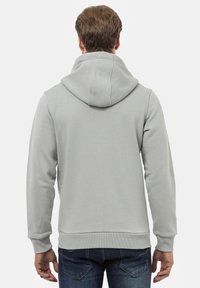 Haut de survêtement zippé gris clair avec une grande capuche, des poignets et un ourlet côtelés. Texture lisse, coupe décontractée, présenté de dos.