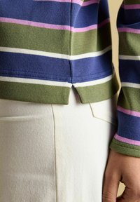 Suurendatud vaade inimesest, kes kannab triibulist pikakäisl hästi särki, millel on sinised, roosad, rohelised ja valged triibud, ning kreemivärvi pükse.