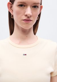 Μπεζ ριμπ T-shirt με στρογγυλή λαιμόκοψη, διαθέτει μικρό κεντημένο λογότυπο σε μπλε, λευκό και κόκκινο στο στήθος.