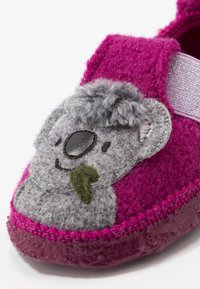 Tofflor i filt i rosa med en grå koaladesign. Har en texturerad ovansida, ett kardborreband och en glänsande lila sula.