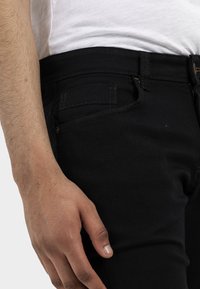 Czarne dżinsy z denimu z bliskim widokiem na pasek, z boczną kieszenią, szlufkami na pasek i kontrastującymi detalami szwów.