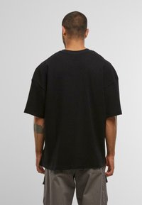 T-shirt noir oversize à manches courtes, texture côtelée, coupe décontractée, col rond, avec des coutures visibles à l'ourlet et de légers motifs de design.