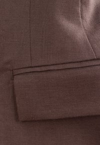 Tissu en lin brun foncé présentant un revers plié avec des coutures visibles et un détail de tissage texturé.