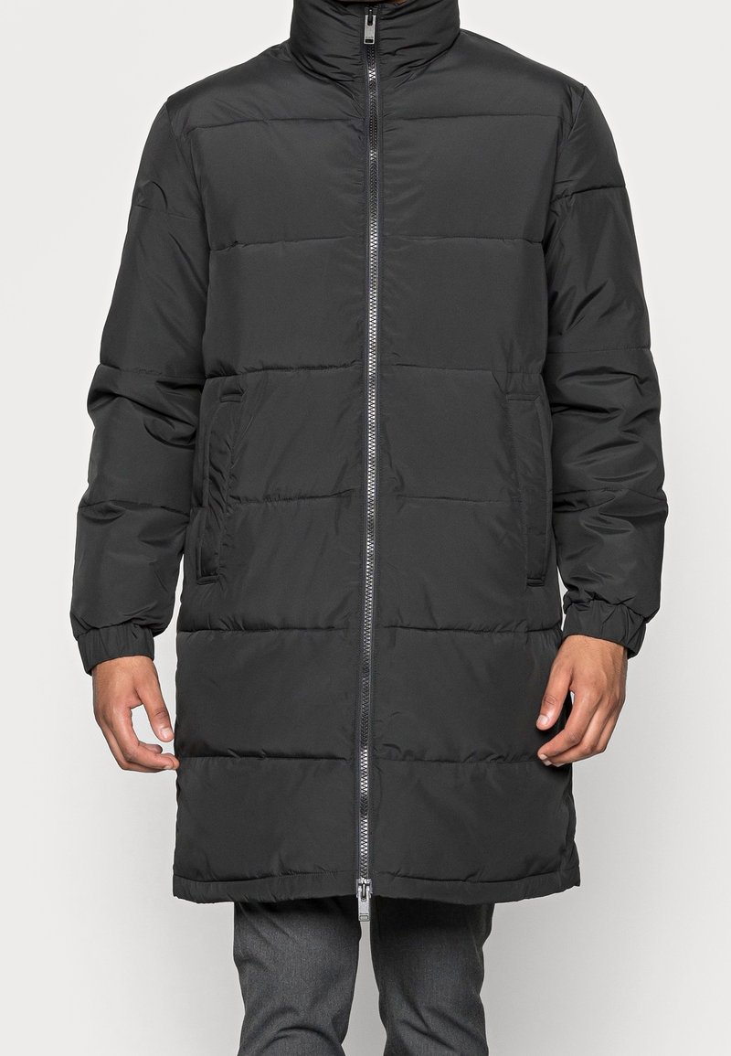 Giubbotto imbottito nero con collo alto, zip frontale, polsini elastici e tasche laterali, caratterizzato da un design trapuntato e una texture morbida e liscia.