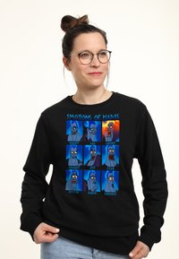 Sudadera negra con paneles gráficos coloridos que muestran diversas emociones de un personaje, etiquetadas: Feliz, Triste, Enojado, Asco, Alegría, Miedo, Emocionado, Aburrido, Sorpresa.