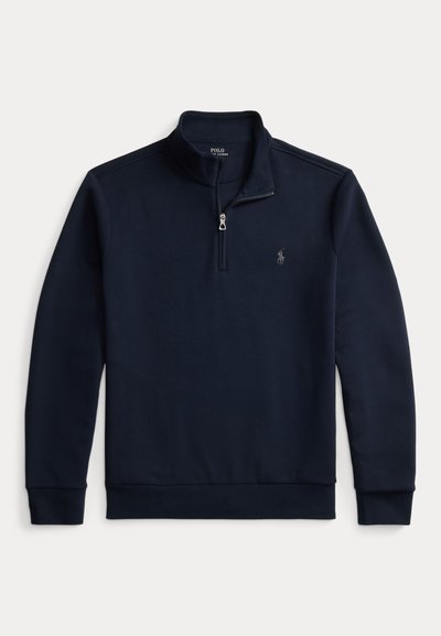 Mørkeblå fleece-pullover med høy krage, glidelås og brodert logo på brystet. Har lange ermer og ribbet hem.