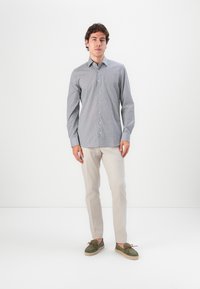 Light blue patterned button-up shirt with long sleeves, paired with beige pants and green slip-on shoes with brown accents.