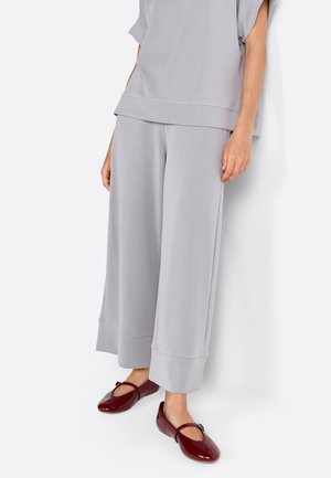 Hallide halli sportlik topp lühikeste varrukatega, koos laia säärega hallide dressipükstega. Jalas on burgundia punased korterjalatsid dekoratiivse aktsendiga. Sile tekstuur.