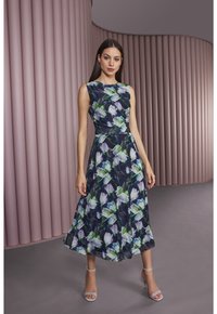Blumenmusterkleid mit tailliertem Oberteil und weit schwingendem Rock. Dunkelblaue Basis, verziert mit weißen und grünen Blumenmustern. Ärmelloses Design.